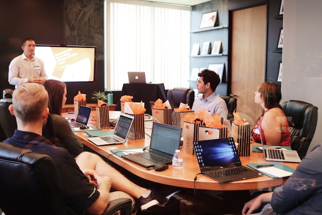 A group of professionals engaged in a discussion in a conference room, with several laptops open on the table, indicating a collaborative work environment.