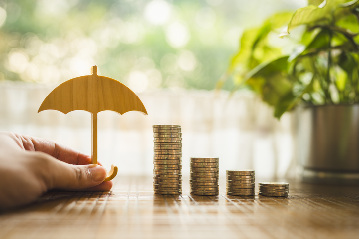 Wooden umbrella shielding stacks of coins, symbolizing the financial security and benefits of an offshore asset protection trust.